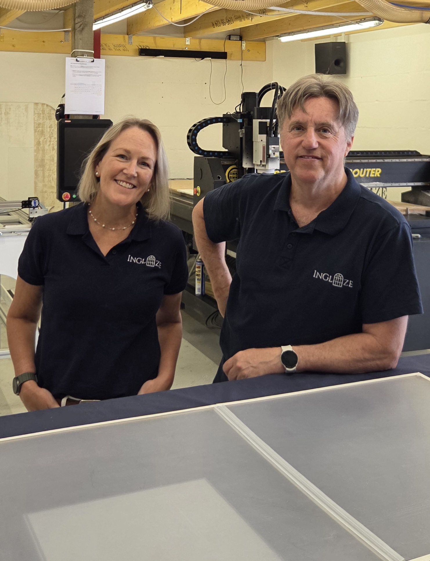 Luci and Campbell Carey, founders of InGlaze, in their Aberdeen workshop with the CNC cutting table and a finished secondary glazing panel.